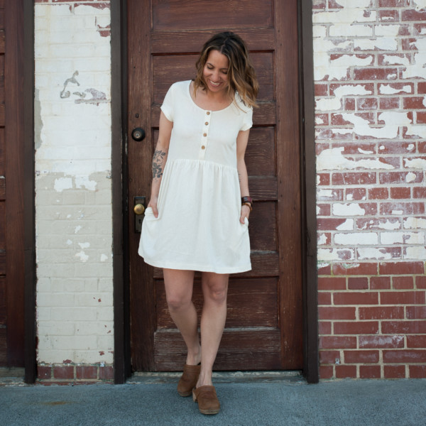 Meg wears a white half placket Hinterland Dress standing in front of a brick wall