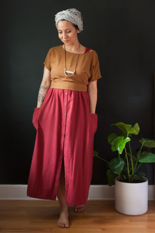 Meg wearing an ochre strata top over a red hinterland dress, standing in front of a black wall