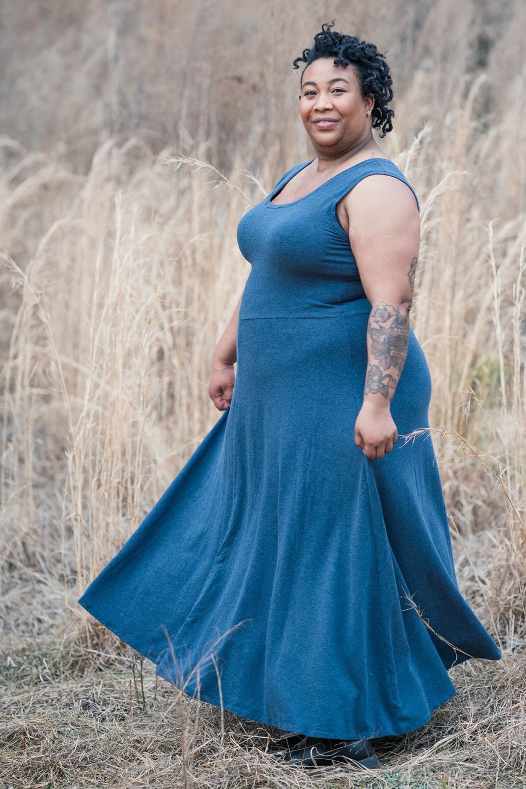 Ashley wears a blue maxi length Stasia Dress standing in the woods