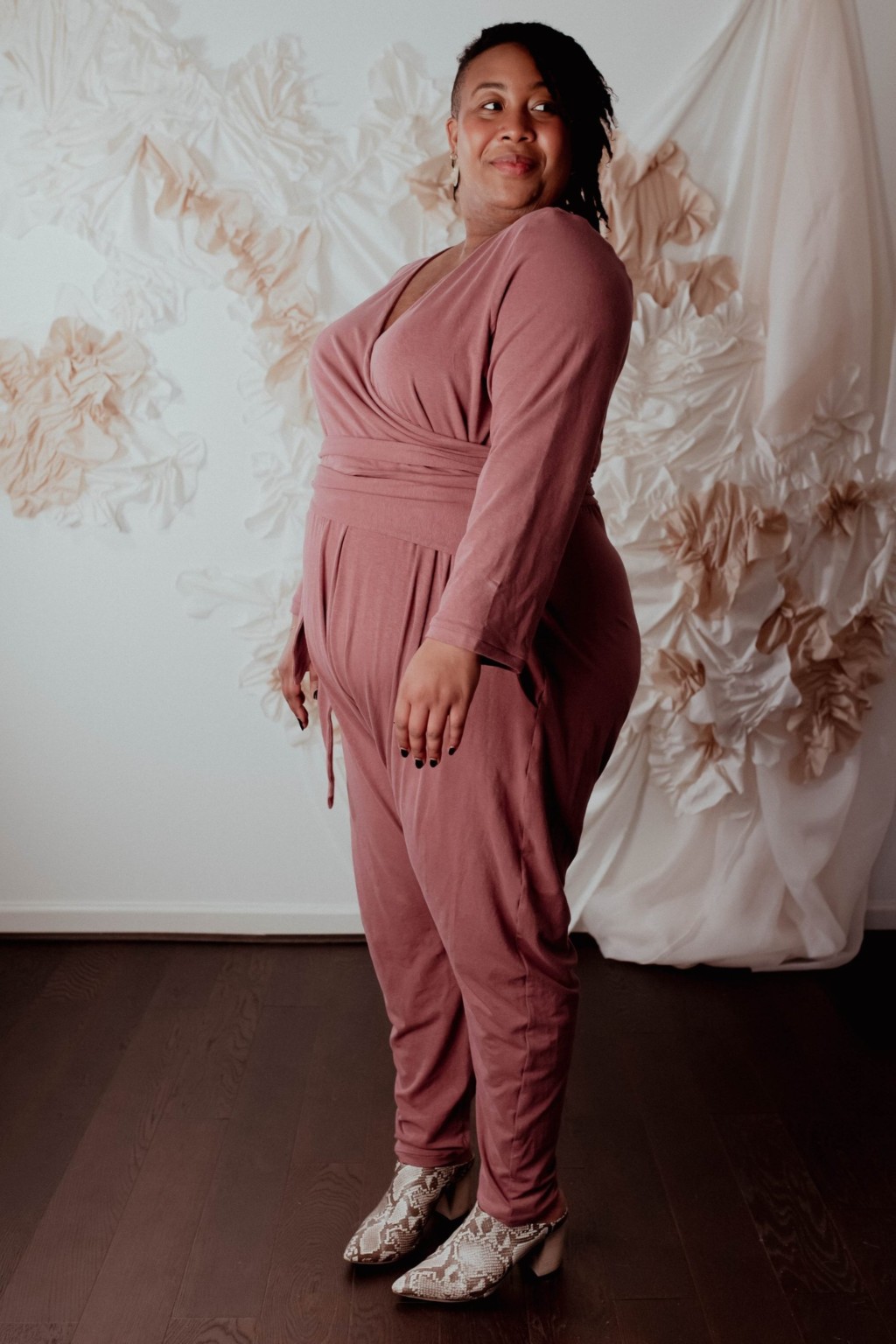 Ashley wears a dusty pink talam jumpsuit, facing to the side at 3/4