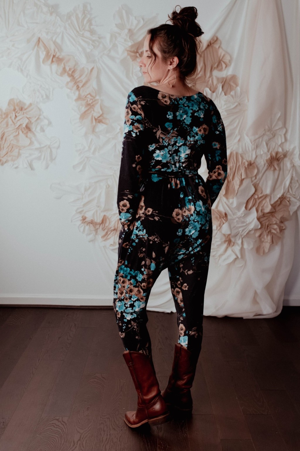 Meg wears a floral talam jumpsuit, facing away from the camera to show off the back