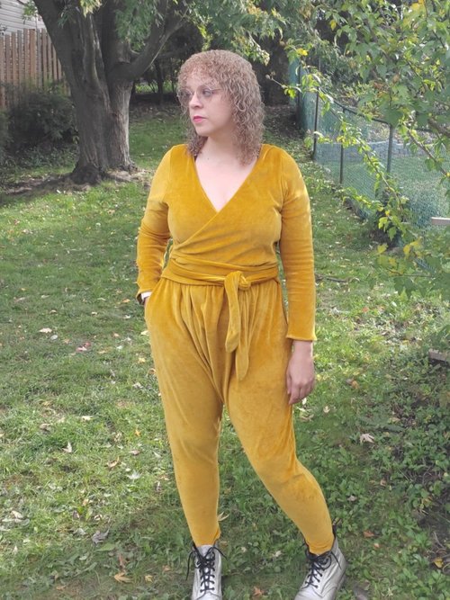Emma wears a yellow gold velour jumpsuit standing in her backyard. 