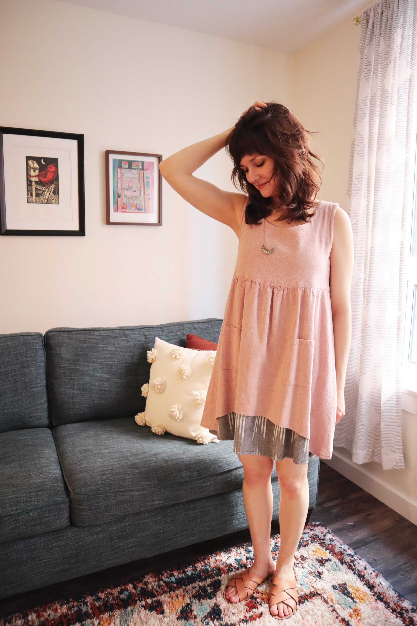 Meredith wears a pink metamorphic dress with a grey ikat underlayer and tan sandals