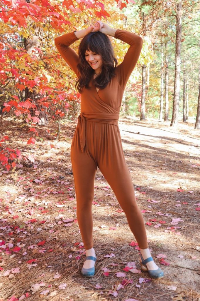 Meredith wears a warm brown jumpsuit in the woods 