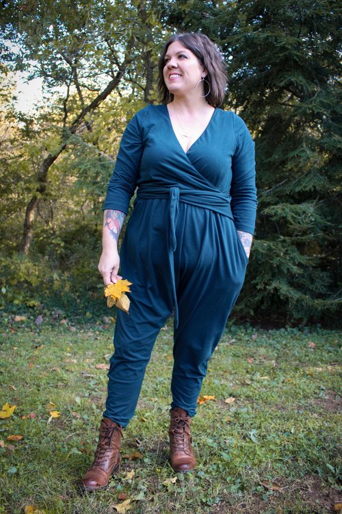Jessica wears a teal jumpsuit standing in the woods. 