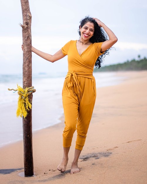 Swetha wears a mustard colored jumpsuit standing on the beach 