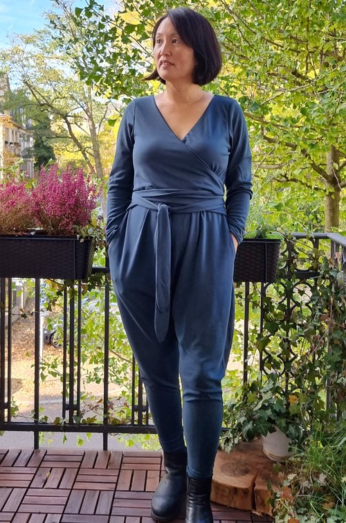 Tania wears a gray blue jumpsuit standing on her porch 