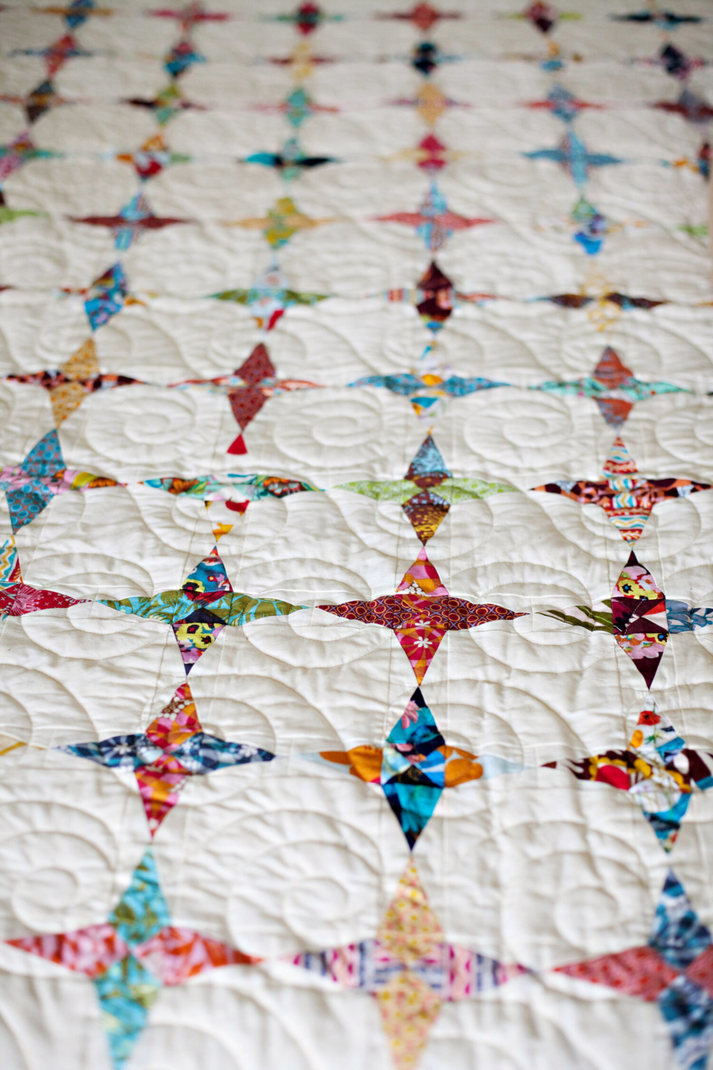 The luminaries quilt in while and multi colored fabric, layed out flate