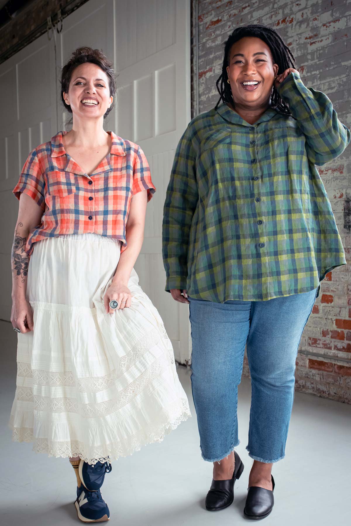 Meg and Ashley wear plaid Joanies, Meg with a white skirt and Ashley with jeans. They smile in front of a brick wall and white door