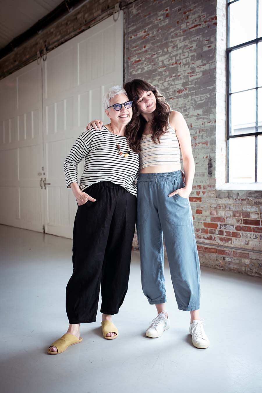 Cindy and Meredith pose together, CIndy wears black chanterelle pants and a striped top, Meredith wears blue chanterelle pants and a striped cami