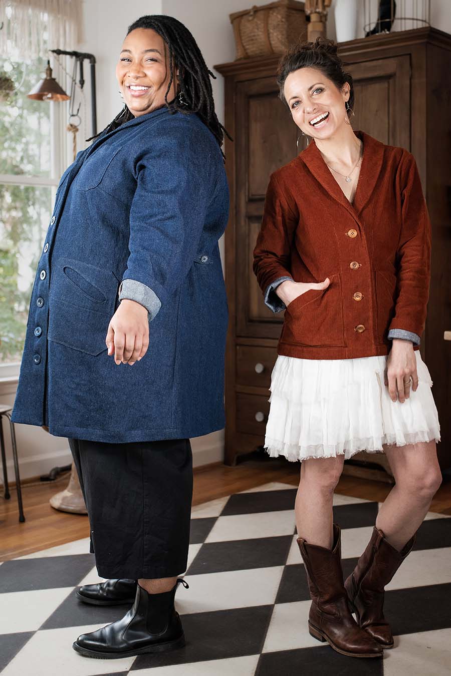 Ashley wears a denim sylvan jacket, standing next to Meg who wear a red corduroy sylvan jacket. They are in Meg's sewing studio. They're both smiling.