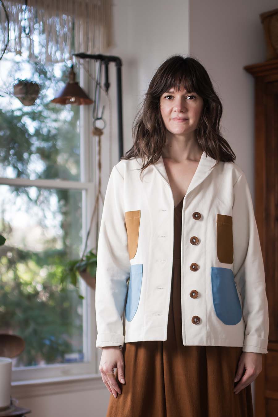 Meredith wears a cream Sylvan with brown and blue pockets, standing in Meg's studio.